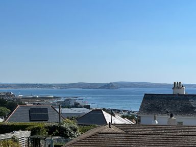 A coastal view with rooftops in the foreground and a body of water with an island and hills in the background at Karenza in Penzance