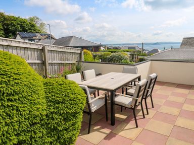An outdoor patio with a dining table and six chairs overlooking rooftops and the sea at Karenza in Penzance