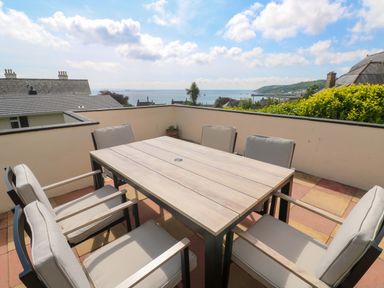 A patio with six cushioned chairs around a wooden table and a sea view at Karenza in Penzance