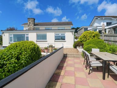 A patio with a table and chairs next to a garden and a white house at Karenza in Penzance