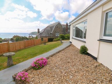 A garden with a gravel path pink flowers a stone birdbath wooden fence and sea view at Karenza in Penzance