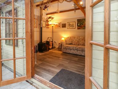 A sitting room with a floral sofa a wood burning stove and framed pictures on the wall at The Cabin at Little Timbers Ringwood