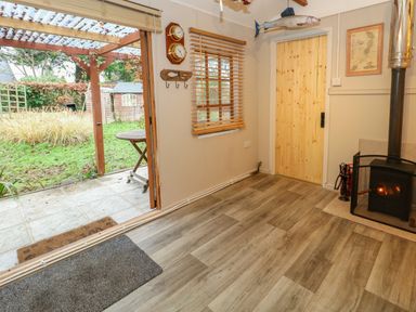 A room with wood flooring a small wood stove a wooden door and an open door leading to a garden at The Cabin at Little Timbers Ringwood