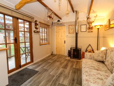 A living room with a sofa wood stove wooden door and glass doors leading outside at The Cabin at Little Timbers in Ringwood