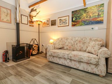 A living room with a wood-burning stove a floral patterned sofa multiple framed pictures on the wall and wood flooring at The Cabin at Little Timbers in Ringwood