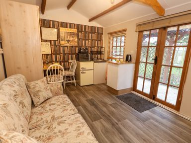 A small living area with a floral sofa a kitchenette with appliances and a dining table with two chairs near wooden French doors at The Cabin at Little Timbers in Ringwood