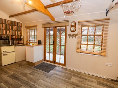 A kitchen area with wooden beams a small fridge microwave toaster sink and windows with blinds at The Cabin at Little Timbers in Ringwood