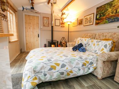 A bedroom with a bed, fireplace, paintings on the wall, and window blinds at The Cabin at Little Timbers in Ringwood