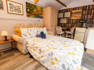 A bedroom with a bed sofa table lamp wardrobe dining table chairs and a small kitchen area with fridge at The Cabin at Little Timbers in Ringwood