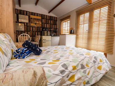 A bedroom with patterned bedspread folded towels a kitchenette with fridge and sink and window blinds at The Cabin at Little Timbers in Ringwood