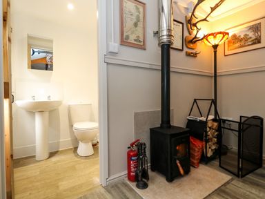 A bathroom with a sink and toilet next to a room with a wood-burning stove firewood and a lamp at The Cabin at Little Timbers in Ringwood