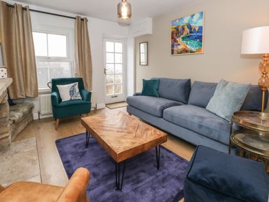 A living room with a blue sofa a green armchair a wooden coffee table and a painting on the wall at Honeypot Cottage in Swanage