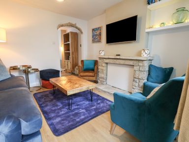 A living room with a blue sofa teal armchairs wooden coffee table stone fireplace and a wall-mounted TV at Honeypot Cottage in Swanage