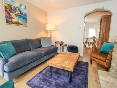 A living room with a blue sofa a wooden coffee table a brown armchair and a floor lamp at Honeypot Cottage in Swanage