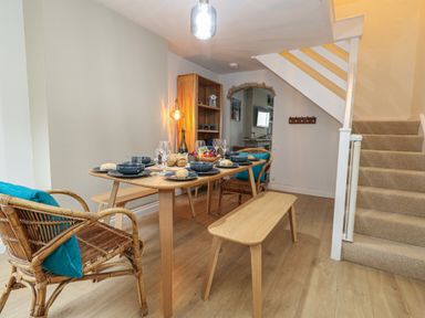 A dining area with a wooden table set with plates and glasses beside carpeted stairs at Honeypot Cottage in Swanage