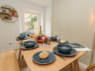 A dining table set with blue plates bowls and wine glasses with a fruit bowl at Honeypot Cottage in Swanage