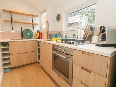 A kitchen with wooden cabinets a gas stove oven a coffee machine and shelves with glassware at Honeypot Cottage in Swanage