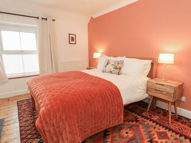 A bedroom with a bed covered in a red quilt and a floral pillow along with wooden bedside tables and lamps at Honeypot Cottage in Swanage