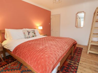 A bedroom with a wooden bed with orange quilt and a bird pillow at Honeypot Cottage in Swanage