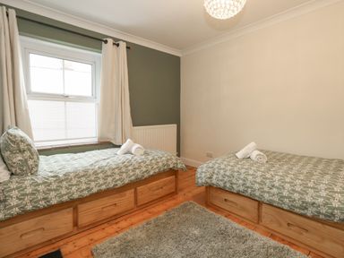 A bedroom with two single beds with green patterned bedding and white rolled towels on wooden floors at Honeypot Cottage in Swanage