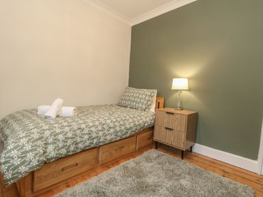 A bedroom with a single bed a nightstand with a lamp and a green wall at Honeypot Cottage in Swanage