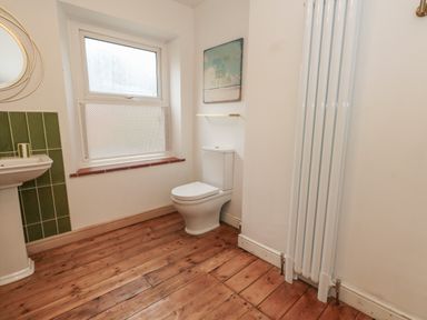 A bathroom with a toilet, pedestal sink, window, wall radiator, and wooden floor at Honeypot Cottage in Swanage