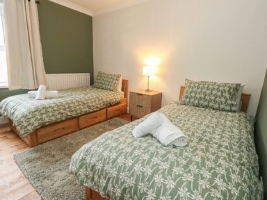 A bedroom with two single beds covered in green floral bedding and a lamp on a wooden nightstand at Honeypot Cottage in Swanage