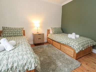 A bedroom with two single beds a wooden nightstand with a lamp and a rug on a wooden floor at Honeypot Cottage in Swanage