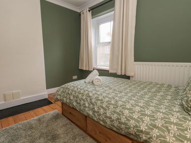 A bedroom with a single bed with floral bedding a rolled towel on the bed a window with curtains and a radiator at Honeypot Cottage in Swanage