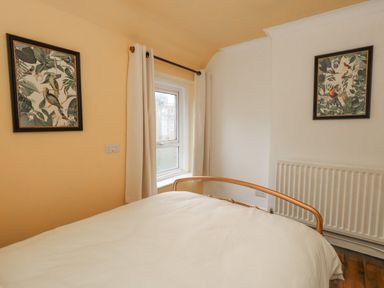 A bedroom with a bed white curtains two framed bird prints and a radiator at Honeypot Cottage in Swanage