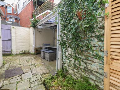 An outdoor patio area with stone flooring wooden gate covered seating area and a stone wall with ivy at Honeypot Cottage in Swanage