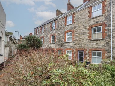 A stone terraced house with multiple windows and doors with surrounding plants and bushes