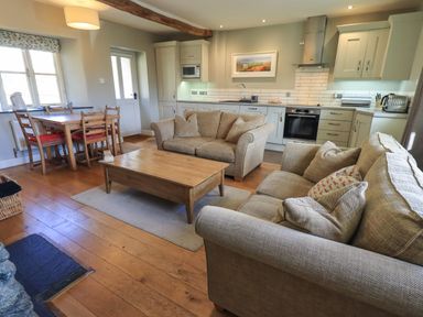 A living area with two beige sofas a wooden coffee table a dining table with chairs and a kitchen with cabinets and appliances at Fox Howe in Thornthwaite