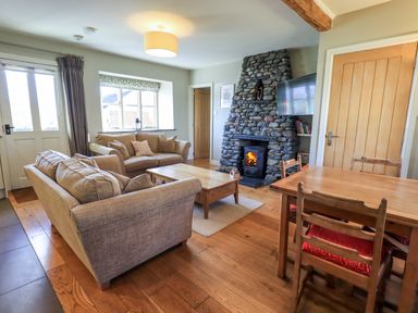 A living room with sofas a stone fireplace a TV a wooden dining table and chairs at Fox Howe in Thornthwaite