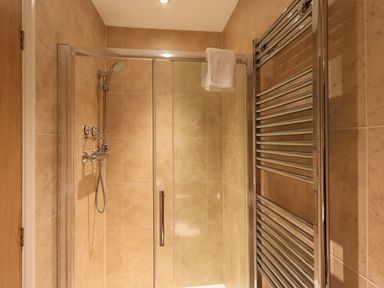 A shower area with glass door and beige tiled walls with a chrome towel rack in a bathroom at Fox Howe in Thornthwaite