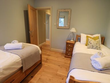 A bedroom with two single beds a bedside table with a lamp a mirror and an open door at Fox Howe in Thornthwaite