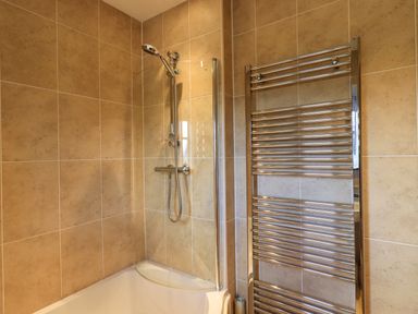 A shower area with a handheld showerhead and a curved glass screen next to a wall-mounted towel radiator in a tiled bathroom at Fox Howe in Thornthwaite