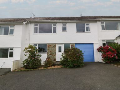 A white two-story house with a blue garage door and bushes in front at Ty Nant in Abersoch