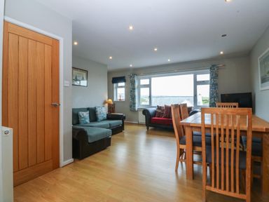 A living room with two sofas a dining table and chairs next to a large window at Ty Nant in Abersoch