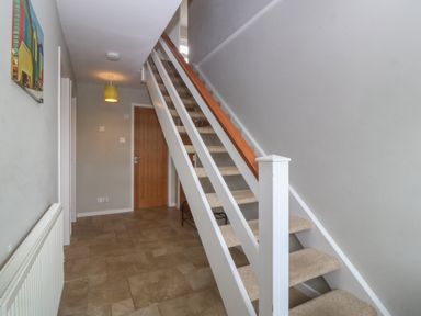 A hallway with tiled floor a staircase with carpeted steps a wooden door and a radiator on the wall at Ty Nant in Abersoch