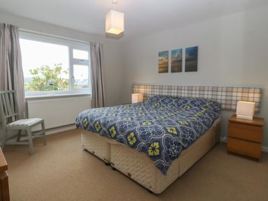 A bedroom with a bed covered with a blue and yellow patterned duvet and two wooden bedside tables with lamps at Ty Nant in Abersoch