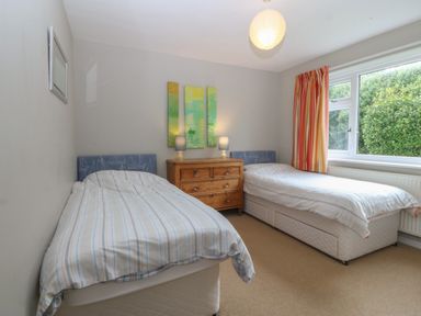 A bedroom with two single beds a wooden chest of drawers with lamps and a window with striped curtains at Ty Nant in Abersoch