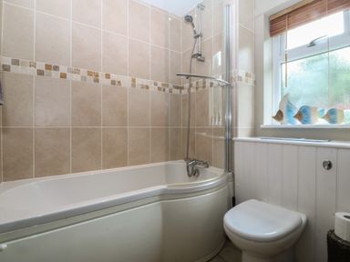 A bathroom with a bathtub shower and a toilet next to a window with fish decorations at Ty Nant in Abersoch