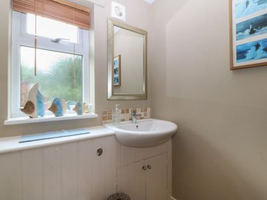 A bathroom with a sink mirror soap dispenser window and fish decorations at Ty Nant in Abersoch