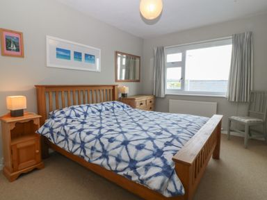 A bedroom with a wooden bed and blue patterned bedding bedside tables with lamps a chest of drawers a window with curtains and a chair at Ty Nant in Abersoch