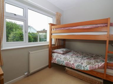 A bedroom with a wooden bunk bed next to a window with yellow check curtains at Ty Nant in Abersoch