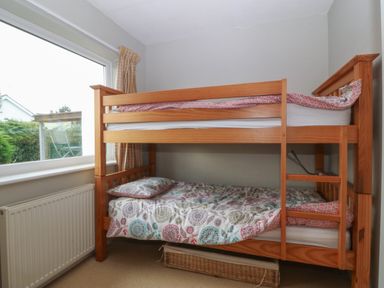 A bedroom with a wooden bunk bed next to a window with a radiator below at Ty Nant in Abersoch