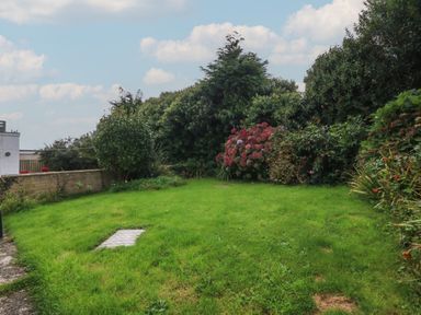 A garden with grass and bushes including pink flowers and a small brick wall at Ty Nant in Abersoch