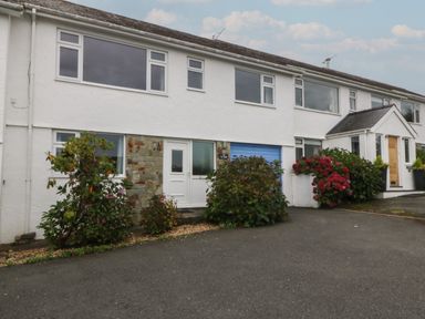 A white two story house with a blue garage door and shrubs in front at Ty Nant in Abersoch