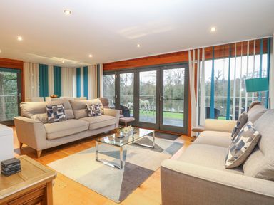 A living room with two beige sofas a glass coffee table and large windows overlooking a river at Tealby in Horning